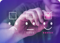 Mão tocando uma tela com três emojis – uma cara triste, uma neutra e outra feliz.