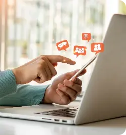 Mão de uma pessoa mexendo no celular em frente ao computador.